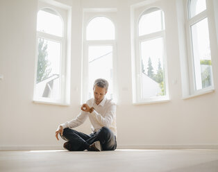 Geschäftsmann sitzt auf dem Boden seines neu renovierten Hauses und prüft die Uhrzeit - KNSF05485