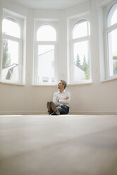 Businessman sitting on ground of his newly refurbished home, looking happy - KNSF05487