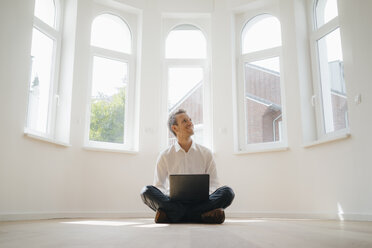 Geschäftsmann sitzt auf dem Boden seines neu renovierten Hauses, benutzt einen Laptop und lächelt - KNSF05488