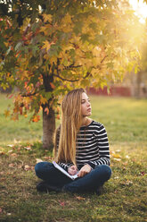 Junge Frau mit Notebook sitzt auf einer Wiese in einem Park im Herbst und macht sich Notizen - LOTF00005