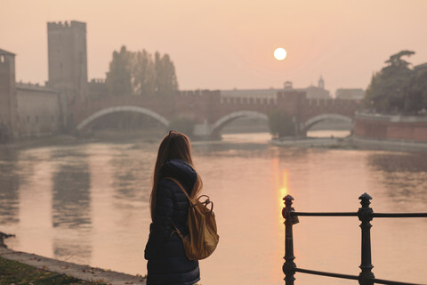 Italien, Verona, Rückenansicht einer Frau mit Rucksack, die die Aussicht bei Sonnenuntergang betrachtet, lizenzfreies Stockfoto