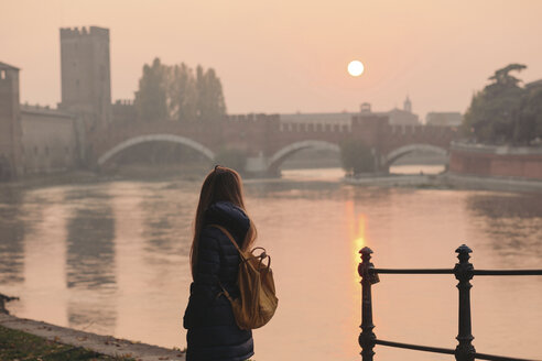 Italien, Verona, Rückenansicht einer Frau mit Rucksack, die die Aussicht bei Sonnenuntergang betrachtet - LOTF00011