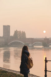 Italien, Verona, Rückenansicht einer Frau mit Rucksack, die die Aussicht bei Sonnenuntergang betrachtet - LOTF00012