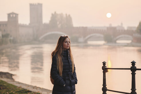 Italy, Verona, portrait of young woman standing in front of River Adige by sunset - LOTF00013
