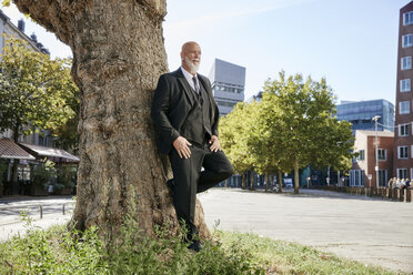 Eleganter Geschäftsmann lehnt an einem Baum in der Stadt und denkt nach - RHF02390