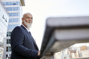 Elegant businessman leaning on railing in the city, looking sceptical - RHF02400