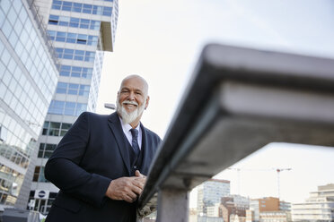 Elegant businessman leaning on railing in the city, smiling - RHF02401