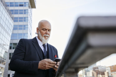 Eleganter Geschäftsmann mit Smartphone in der Stadt - RHF02402