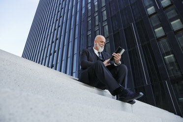 Eleganter Geschäftsmann, auf einer Treppe in der Stadt sitzend, mit digitalem Tablet - RHF02424