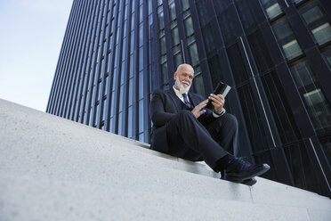 Eleganter Geschäftsmann, auf einer Treppe in der Stadt sitzend, mit digitalem Tablet - RHF02425