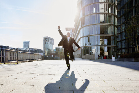 Businessman running in the city, raising hand, celebrating his success stock photo