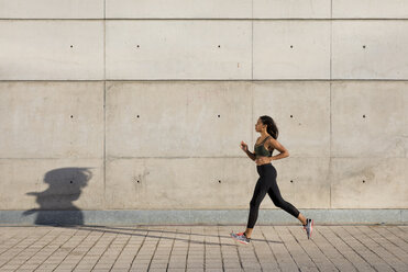 Young woman running along concrete wall in the city - MAUF02150