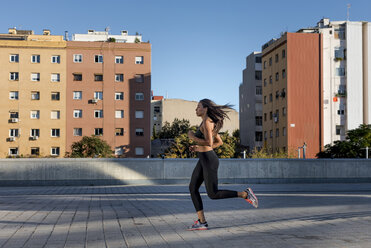 Young woman running along apartment blocks in the city - MAUF02152
