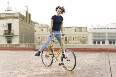 Porträt einer glücklichen jungen Frau, die auf einem Fahrrad in der Stadt balanciert - ERRF00427