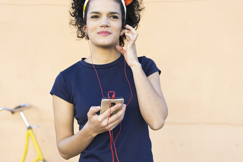 Lächelnde junge Frau mit Smartphone beim Musikhören - ERRF00431