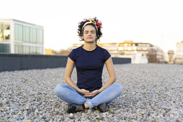 Young woman with closed eyes sitting on roof terrace in the city at sunset - ERRF00437