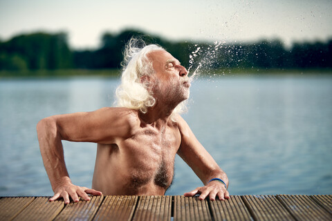 Senior man with white hair leaning on jetty splashing with water stock photo