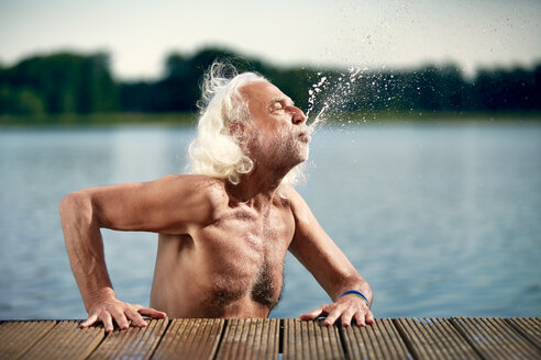 Senior man with white hair leaning on jetty splashing with water - VWF00023