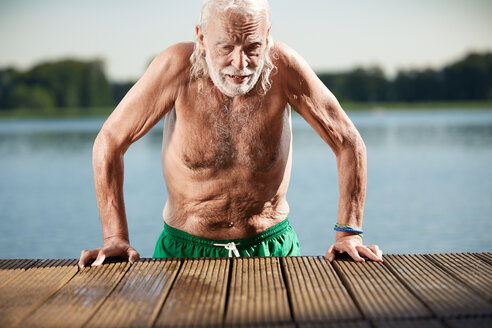 Portrait of senior man leaning on jetty at lake - VWF00024