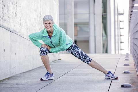 Portrait of smiling mature woman stretching in the city stock photo