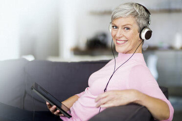 Porträt einer glücklichen reifen Frau, die mit einem digitalen Tablet auf der Couch sitzt und mit Kopfhörern Musik hört - VWF00044