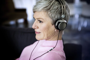 Zufriedene reife Frau, die zu Hause mit Kopfhörern Musik hört - VWF00046