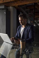 Confident businessman using cell phone and laptop in a studio loft - MAUF02184