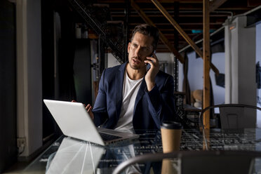 Geschäftsmann mit Laptop und Mobiltelefon in einem Loft-Studio - MAUF02187