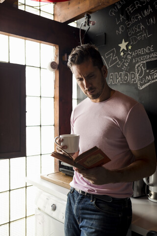 Mann mit Tasse Kaffee liest ein Buch in der Küche, lizenzfreies Stockfoto