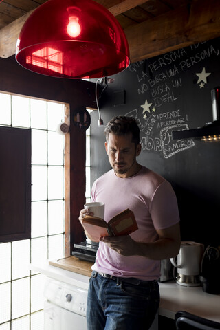 Mann mit Tasse Kaffee liest ein Buch in der Küche, lizenzfreies Stockfoto