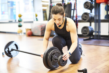 Fitness instructor putting weights on barbell in gym - AURF08116