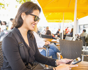 Frau, die in einem Straßencafé eine SMS auf ihrem Smartphone schreibt, Köln, Nordrhein-Westfalen, Deutschland - AURF08137