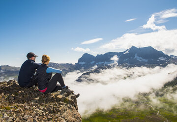 Couple looking at view of mountains rising above fog, Borgafjordur Eystri, Iceland - AURF08210