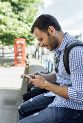UK, London, lächelnder Mann benutzt sein Smartphone auf der Straße - MGOF03901