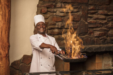 Smiling cook cooking in kitchen with burning frying pan - ZEF16119