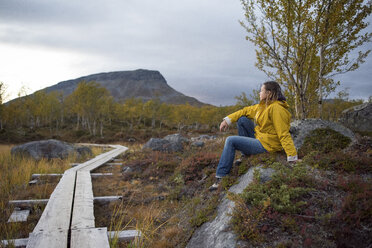 Finland, Lappland, Kilpisjaervi, woman sitting at wooden boardwalk - PSIF00200