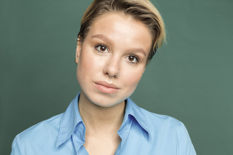 Porträt einer jungen Frau mit Nasenpiercing vor grünem Hintergrund, lizenzfreies Stockfoto