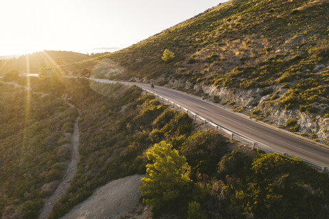 Italien, Insel Elba, Radfahrer auf Küstenstraße gegen die Sonne, Luftaufnahme mit Drohne, lizenzfreies Stockfoto