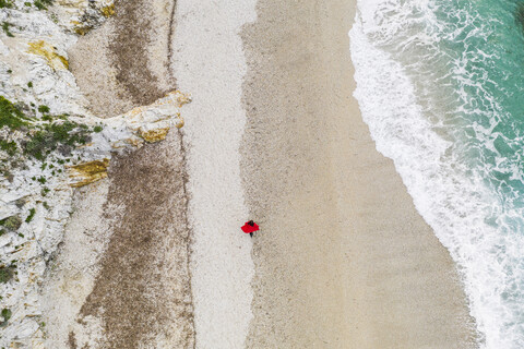 Italien, Elba, Frau mit rotem Mantel bei Strandspaziergang, Luftaufnahme mit Drohne, lizenzfreies Stockfoto