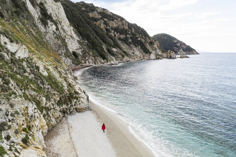 Italien, Elba, Frau mit rotem Mantel bei Strandspaziergang, Luftaufnahme mit Drohne, lizenzfreies Stockfoto