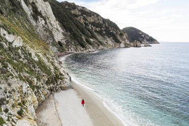 Italy, Elba, woman with red coat walking at beach, aerial view with drone - FBAF00221