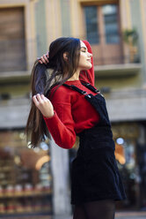 Modische junge Frau in rotem Strickpullover und schwarzem Trägerkleid in der Stadt - JSMF00720