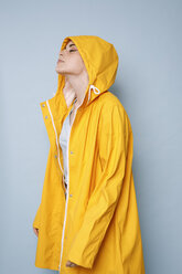 Young woman wearing yellow rain coat in front of blue background - GRSF00047