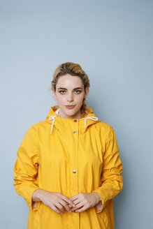 Porträt einer jungen Frau mit gelbem Regenmantel vor blauem Hintergrund - GRSF00051
