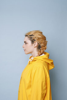 Profil einer jungen Frau mit gelbem Regenmantel vor blauem Hintergrund - GRSF00054
