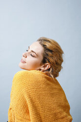 Smiling young woman wearing yellow knitwear in front of blue background - GRSF00056