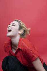 Lachende junge Frau vor rotem Hintergrund - GRSF00062