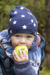 Porträt eines kleinen Jungen in einer Babytrage, der einen Apfel isst - TCF06060