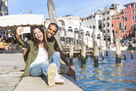 Italien, Venedig, verspieltes Paar entspannt sich und macht ein Selfie mit der Rialto-Brücke im Hintergrund, lizenzfreies Stockfoto