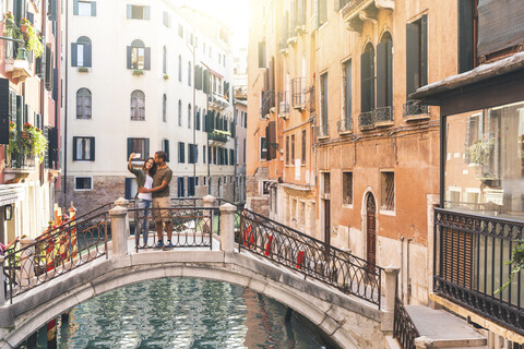 Italien, Venedig, junges Paar steht auf einer kleinen Brücke und macht ein Selfie, lizenzfreies Stockfoto